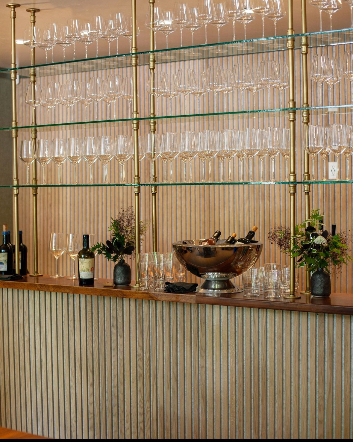 Soil & Oak custom built bar setup with wine glasses, bottles, and decor against a striped wall.