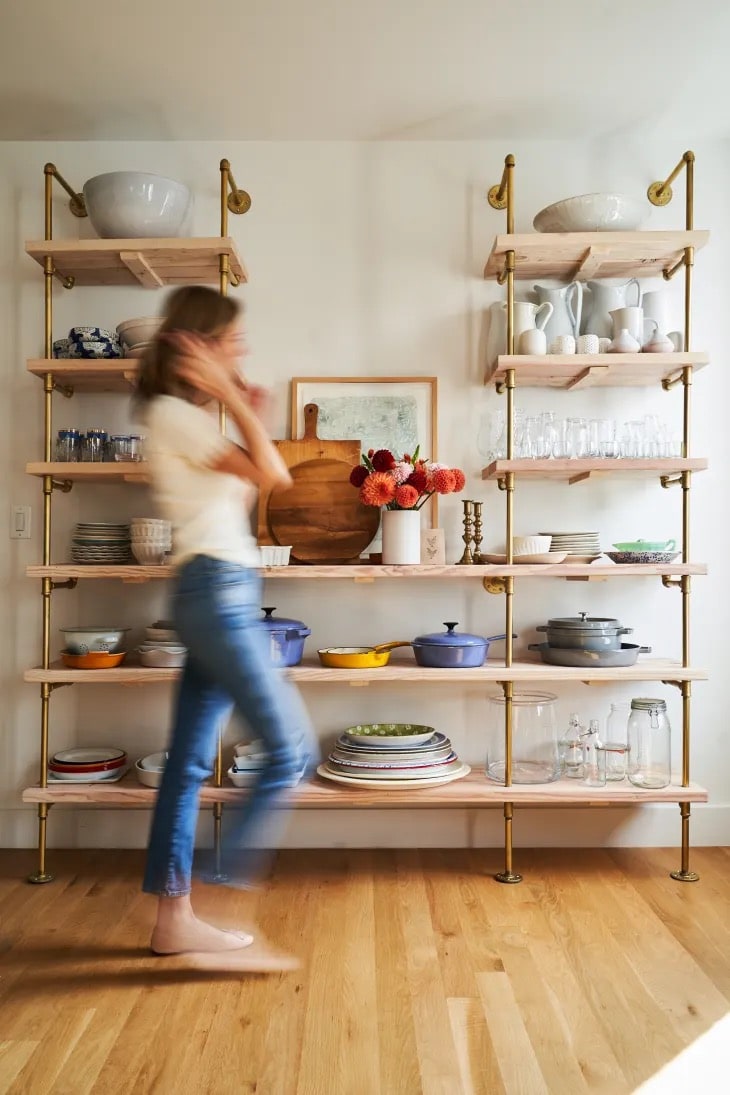 woman walking past custom bookshelves with brass plated pipes and maple shelves | Soil & Oak