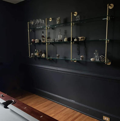 Kitchen and bar glass shelves with gold piping on a black wall in billiards room | Soil & Oak