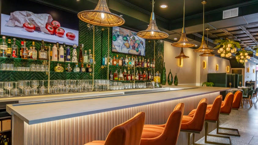 Modern bar interior built by Soil & Oak with orange chairs, shelves of drinks, and hanging lights.