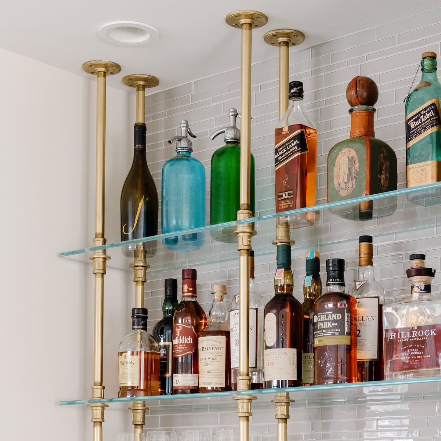 close up photo ceiling mounted bar and kitchen shelving with brass plated pipes and glass shelves in white tiled bar | Soil & Oak