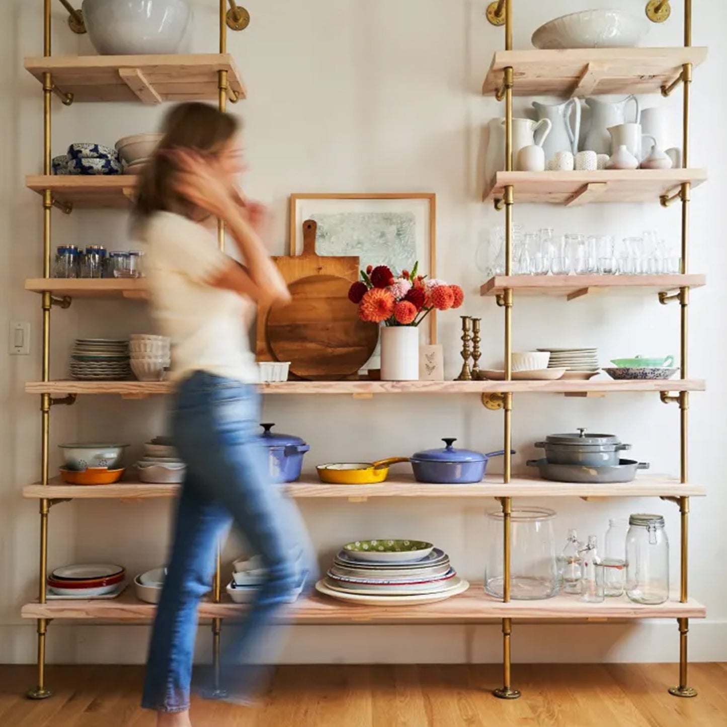 Woman walking by kitchen bookshelf with brass plated pipes and natural maple shelves | Soil & Oak