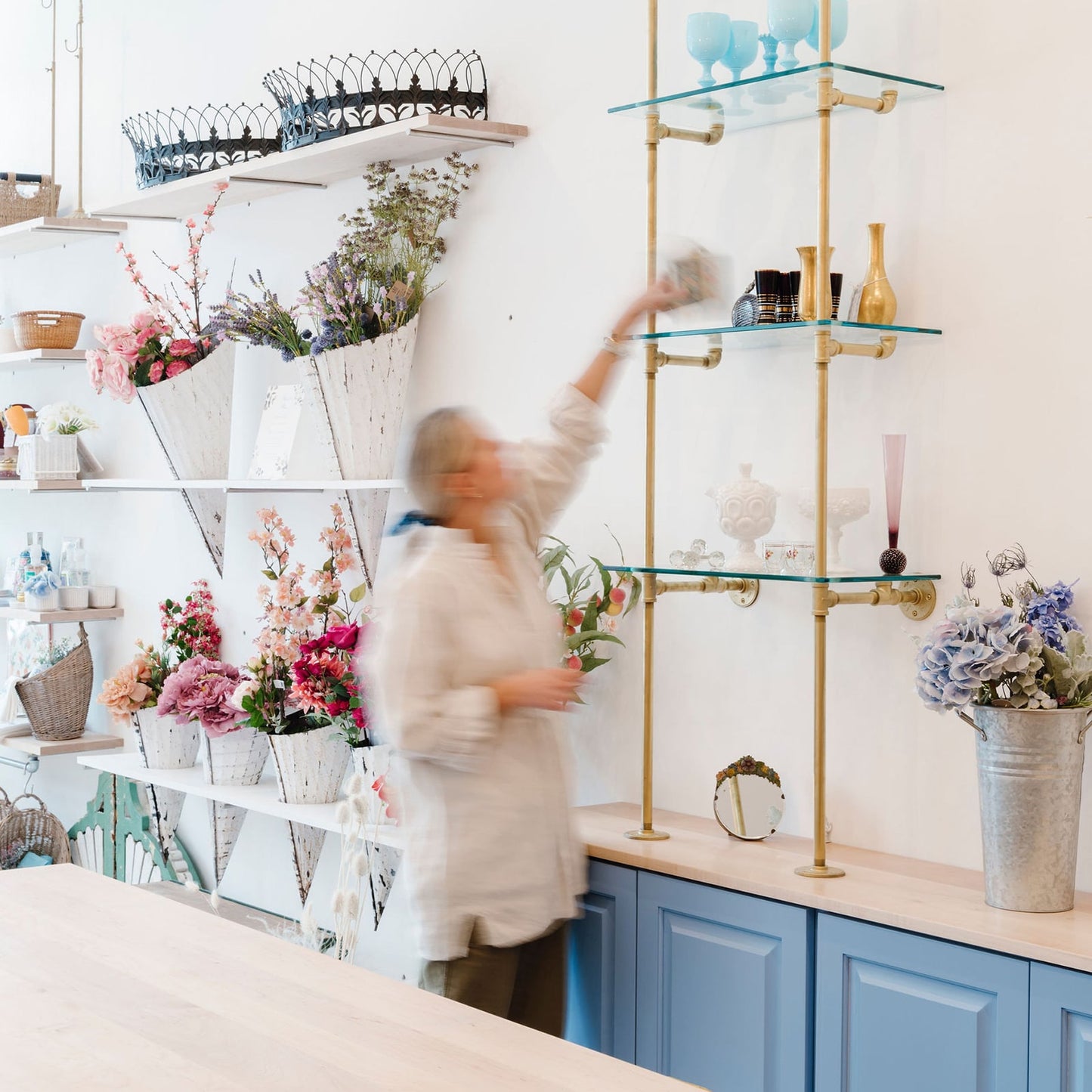 woman placing items on custom retail shelving units with brass plated pipes and glass shelves | Soil & Oak