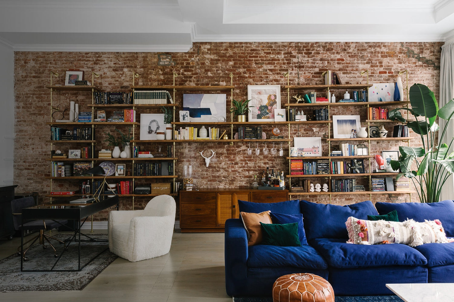 custom bookshelves with brass plated pipes and walnut shelves with a bar unit on a brick wall in a room designed by Tali Roth
