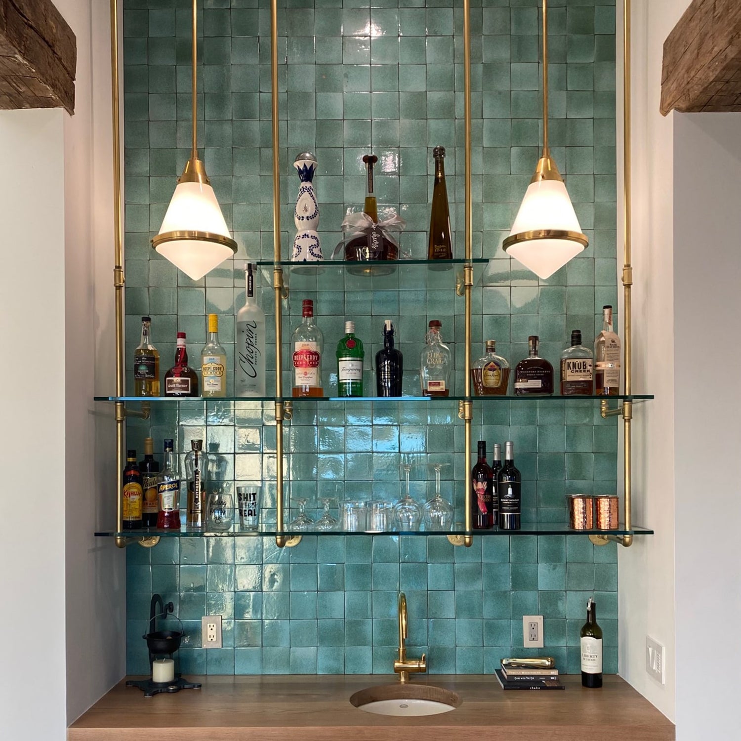 ceiling to wall kitchen and bar unit with brass pipes and glass shelves holding bottles of liquor in a home kitchen