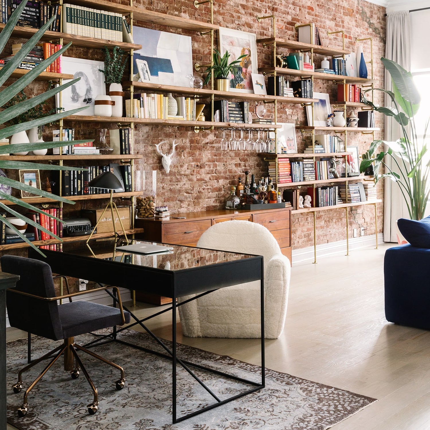 Beautiful custom wall mounted shelves with wood and gold pipes in an open floor design along a brick wall | Soil & Oak