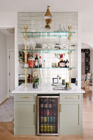 counter to wall kitchen and bar unit with gold piping and glass shelves in front of a mirrored wall and marble countertop