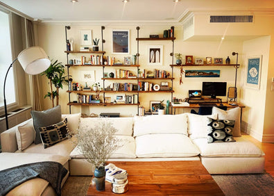 Wall mounted oak shelves with black piping, and a built in desk in a light colored living room | Soil & Oak