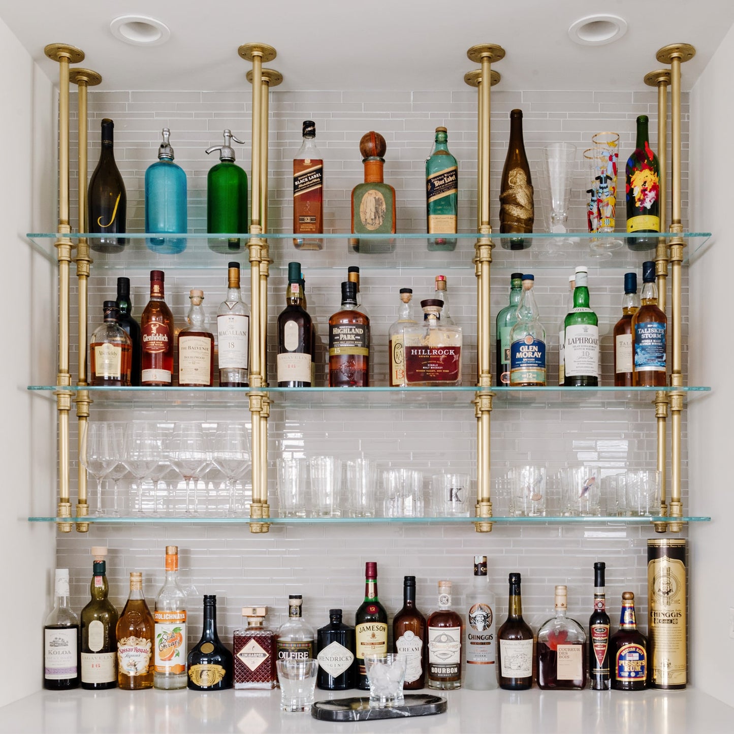 soil & oak ceiling mounted bar and kitchen shelving with brass plated pipes and glass shelves in white tiled bar
