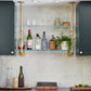 small ceiling to wall kitchen shelving with brass plated pipes and glass shelves in between two cabinets | Soil & Oak 