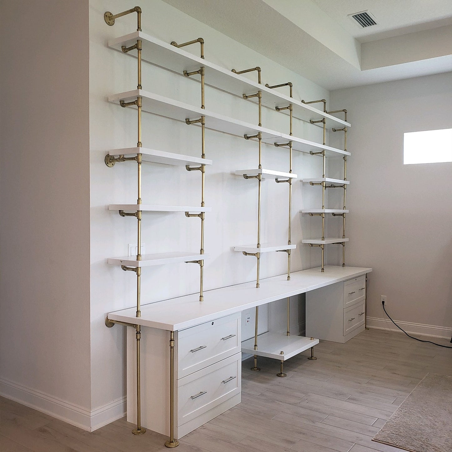 custom soil & oak bookshelf and built-in desk with brass plated pipes and white painted wood shelves