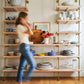 Woman walking by kitchen bookshelf with brass plated pipes and natural maple shelves | Soil & Oak 